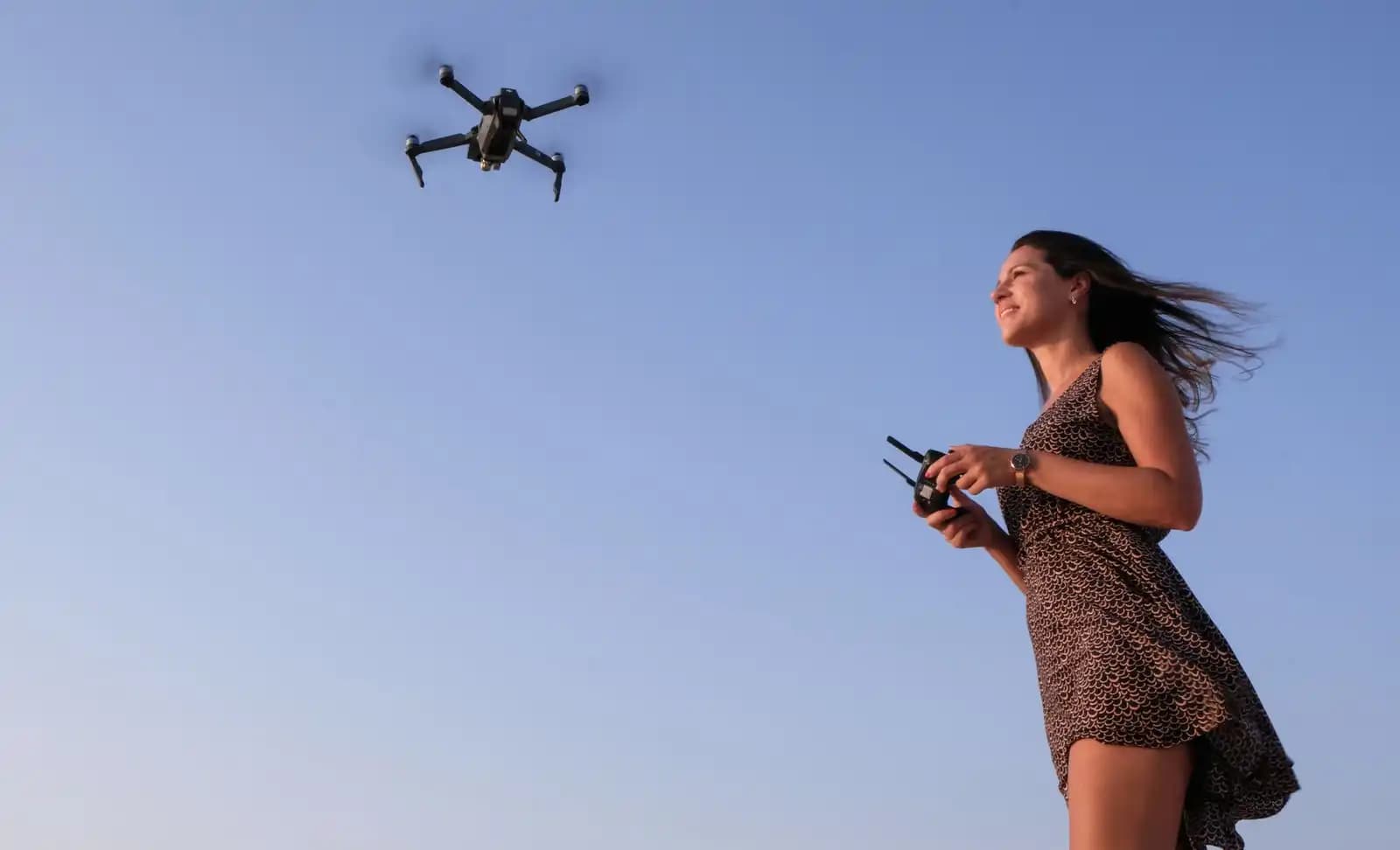 Seorang remote pilot profesional sedang menerbangkan drone di area lapang berangin
