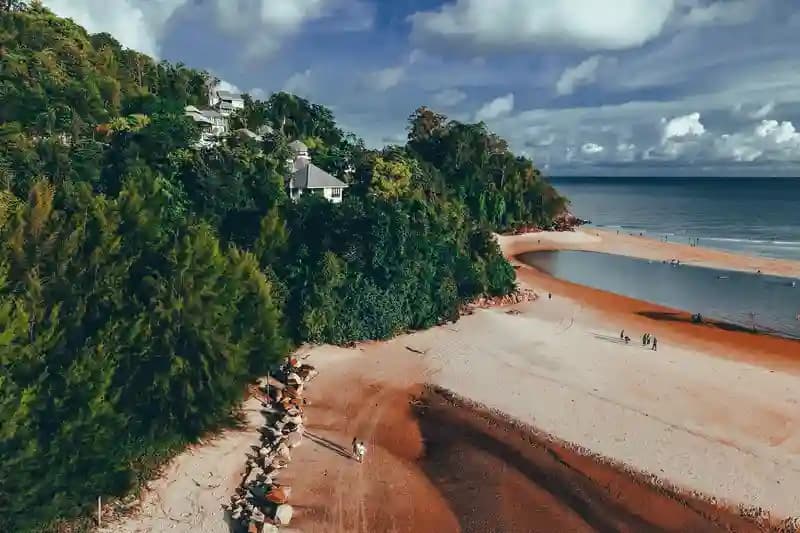 Drone terbang di atas pantai tropis dengan pemandangan pegunungan dan laut biru jernih.